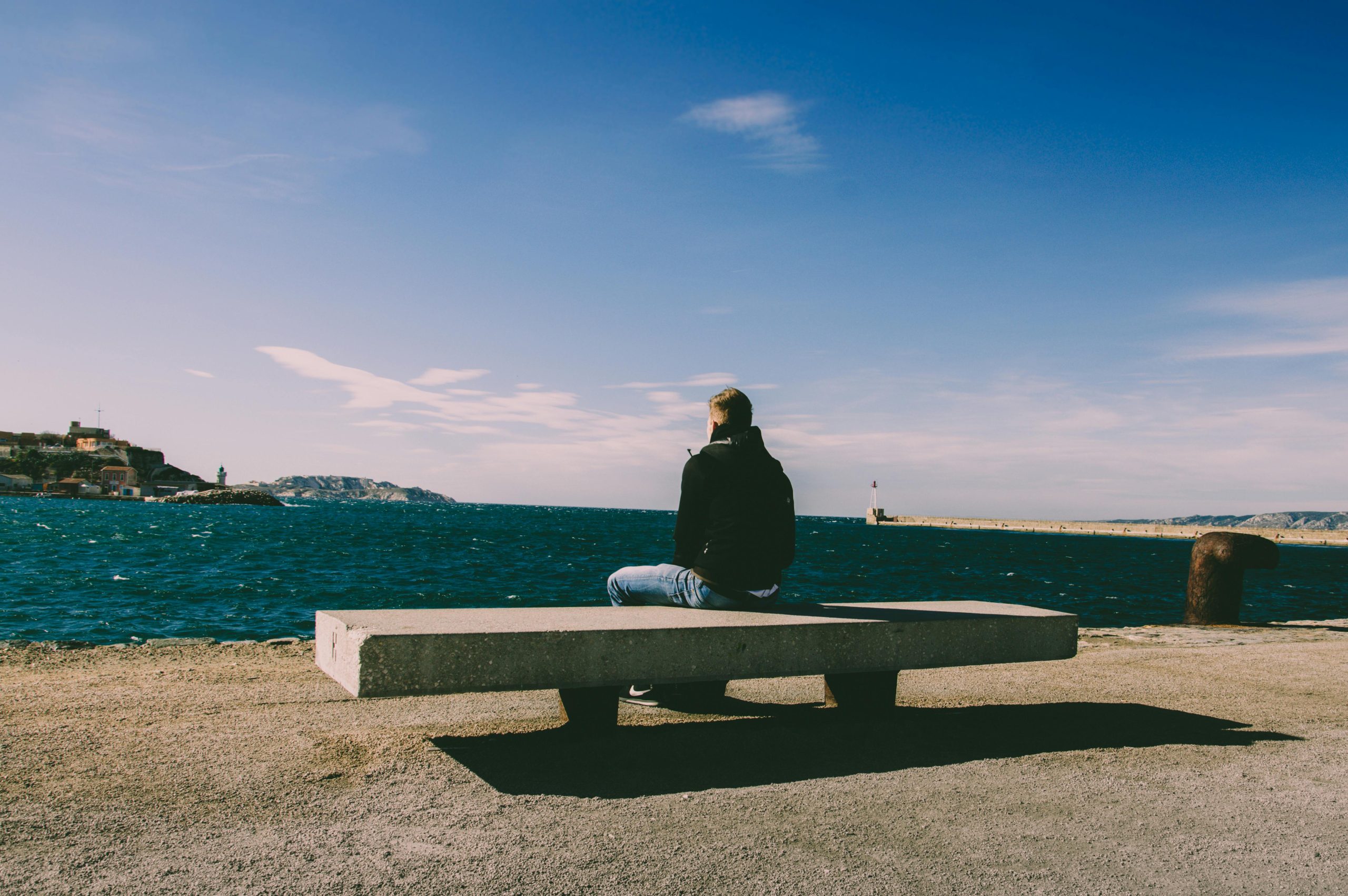Person sitting alone on a bench by the sea, facing away